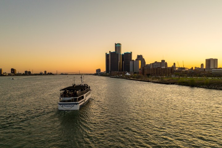 Boat on a river heading towards a city skyline at sunset.