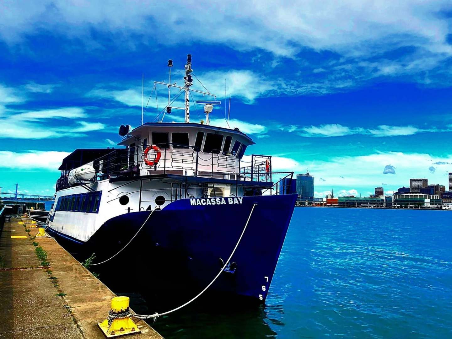 A boat docked by a cityscape under a partly cloudy blue sky.