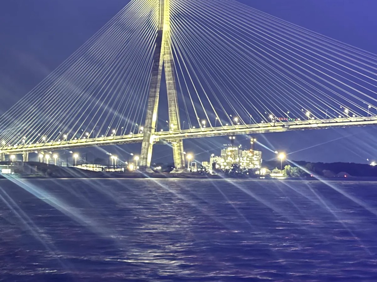 Illuminated cable-stayed bridge over water at night, with lights reflecting on the surface.